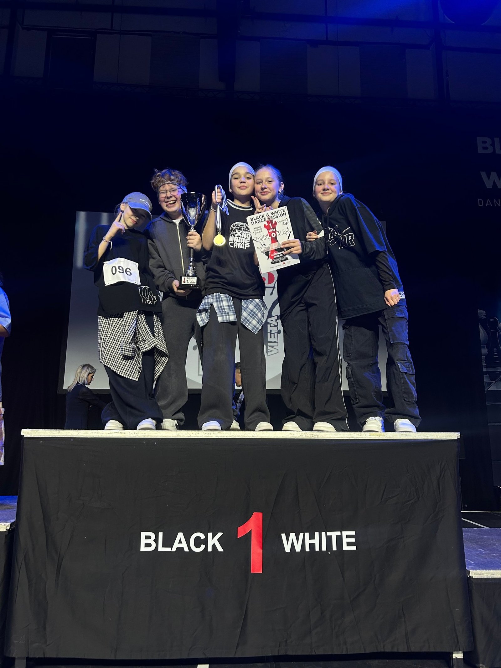 Young hip hop dance crew celebrating on stage with a first place trophy and gold medal.